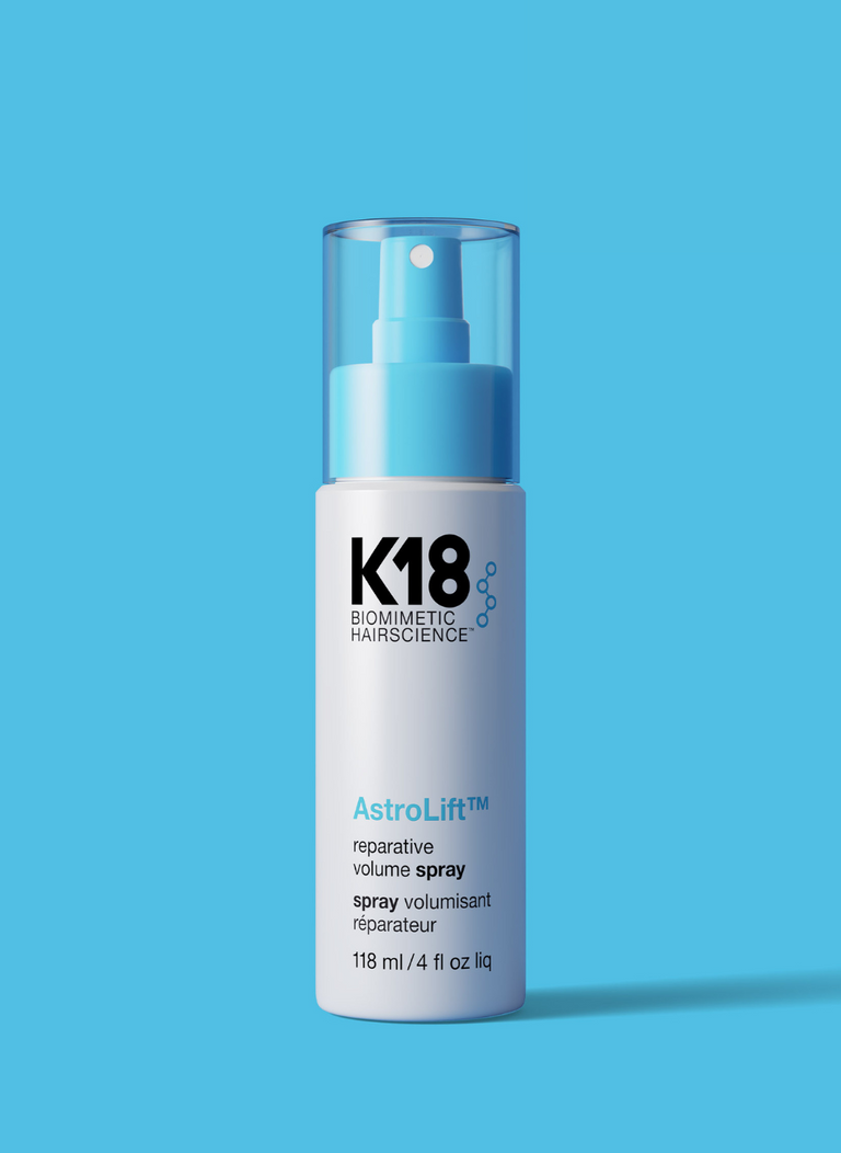 White and light blue bottle of Astrolift reparative volume spray on a blue background.